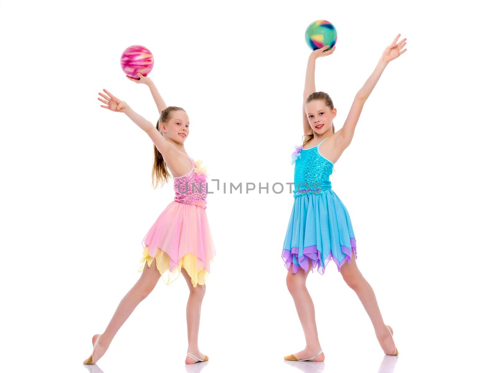 Two cheerful little girls gymnasts in competitions, perform exercises with the ball. The concept of children's sports, fitness, healthy lifestyle. Isolated on white background.