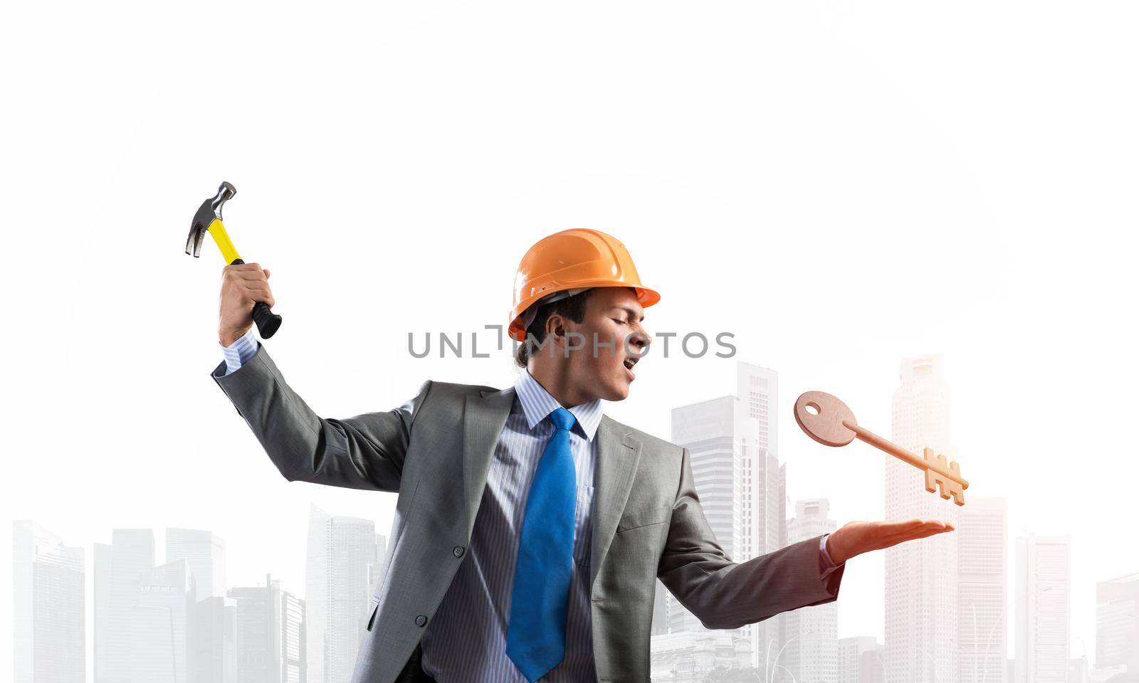 Furious businessman going to crash with hammer steel key. Young handsome contractor in business suit and safety helmet standing on cityscape background. Financial crisis and bankruptcy in real estate