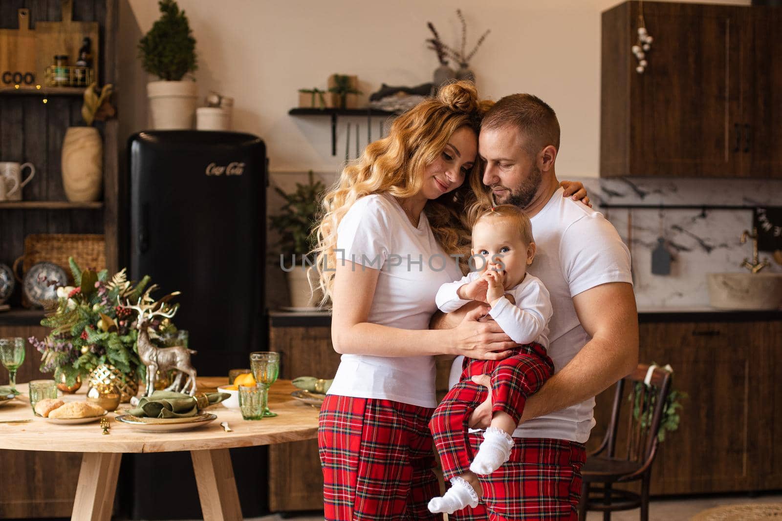 Happy couple holding cute baby while hugging in their home. Christmas holiday concept