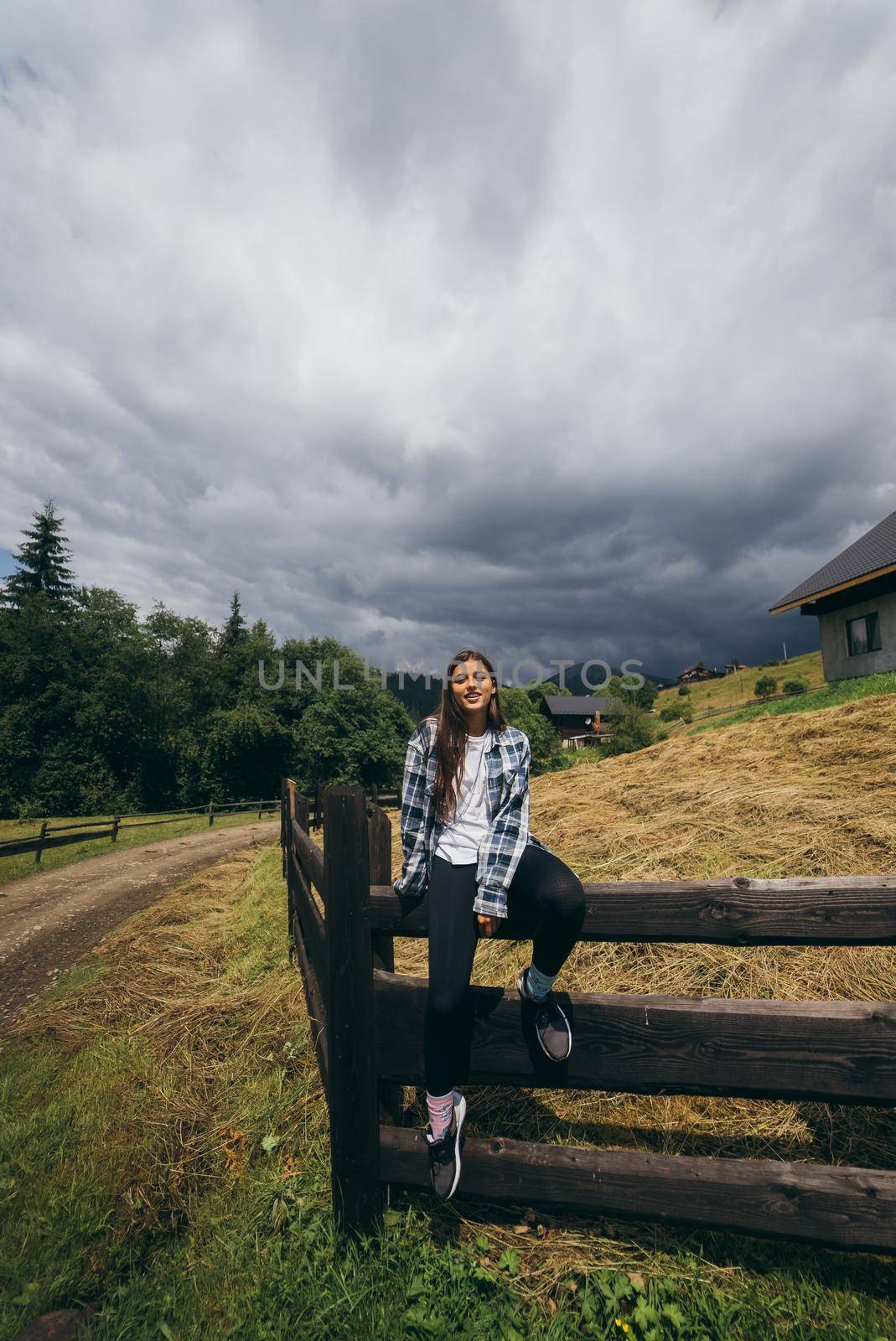 A young attractive Caucasian female sitting on a fence and posing at camera