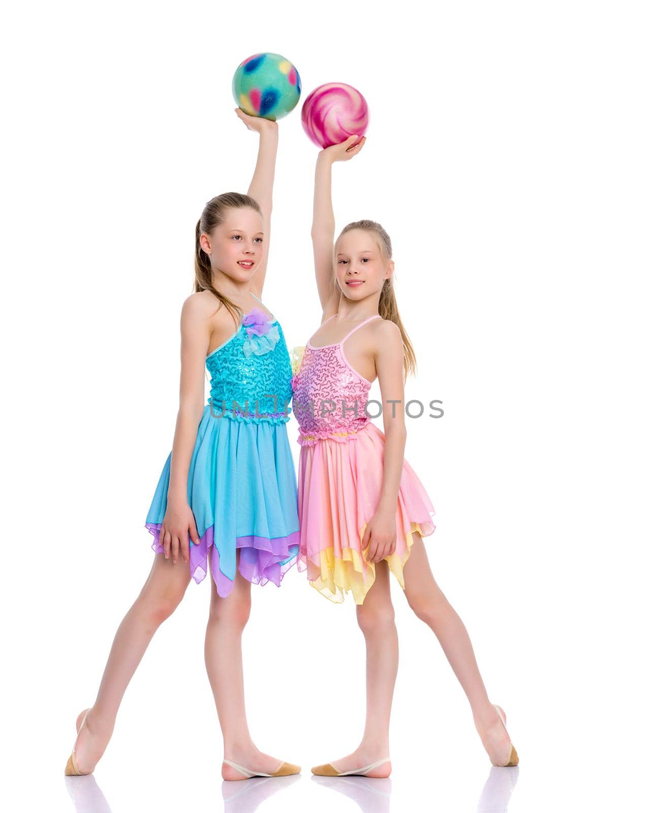 Two cheerful little girls gymnasts in competitions, perform exercises with the ball. The concept of children's sports, fitness, healthy lifestyle. Isolated on white background.