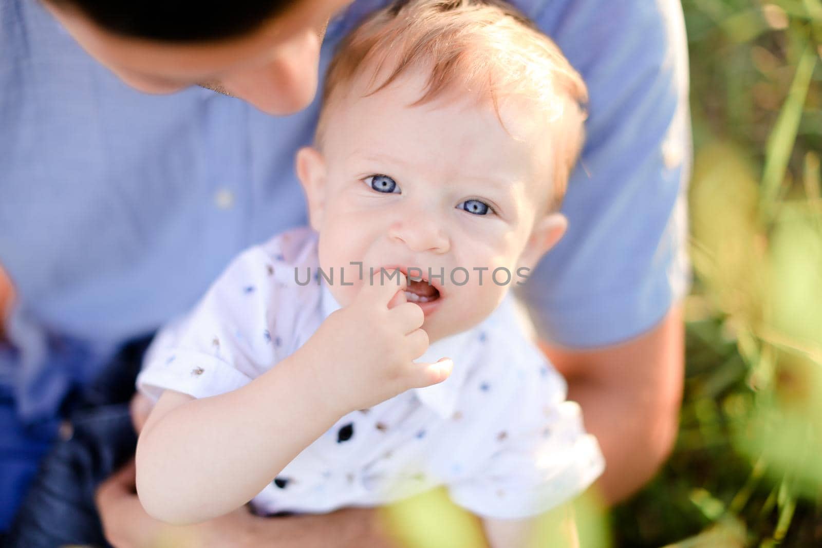 Closeup portrait of little male baby on father blue t shirt background. Concept of childhood.