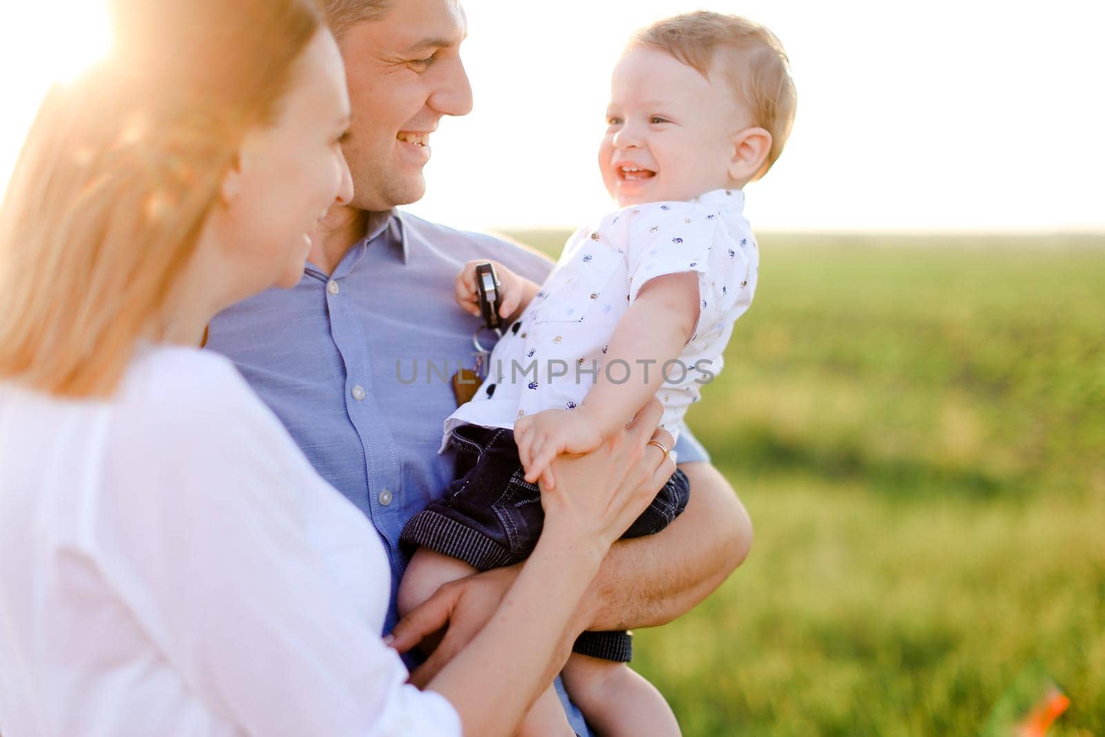 Young mother and father holding baby, grass in background. Concept of nature and parenthood.
