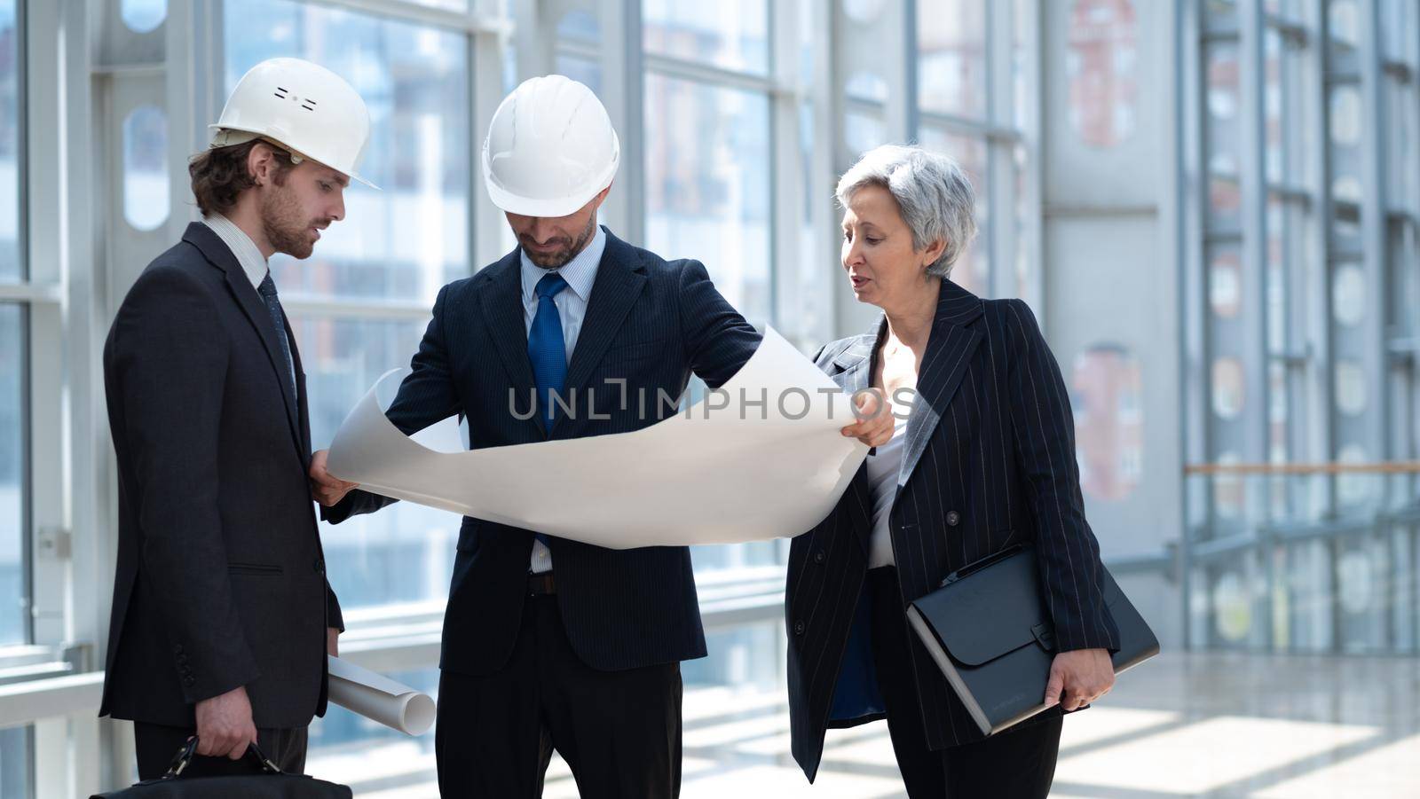 Multi ethnic business architect people in safety helmets discussing blueprint standing in the lobby at office