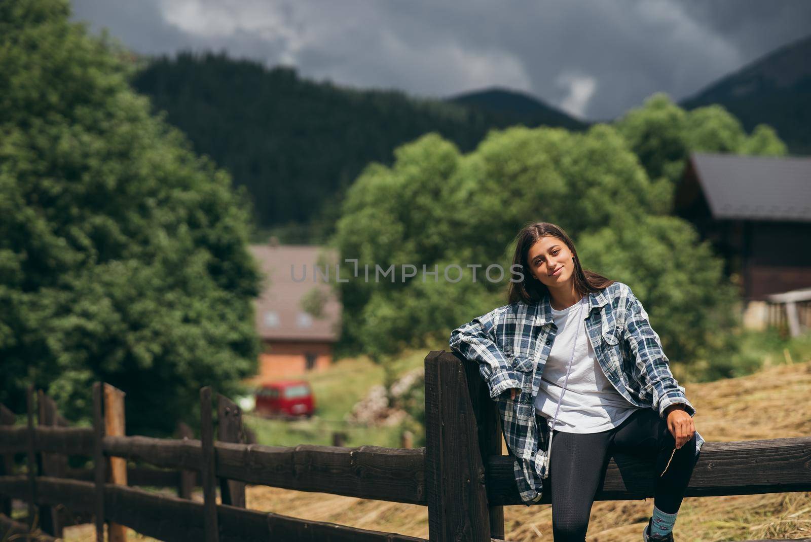 A young attractive Caucasian female sitting on a fence and posing at camera