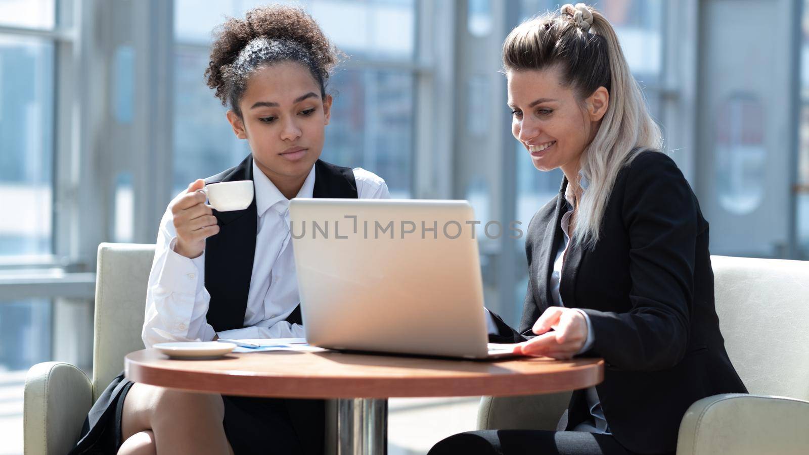 Two business women in modern office building cafe working with laptop