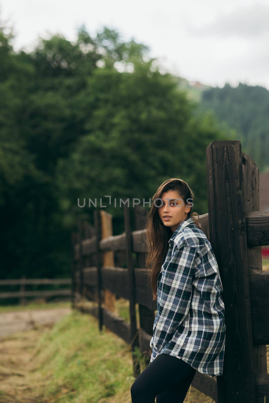 A young attractive Caucasian female stand by a fence and posing at camera