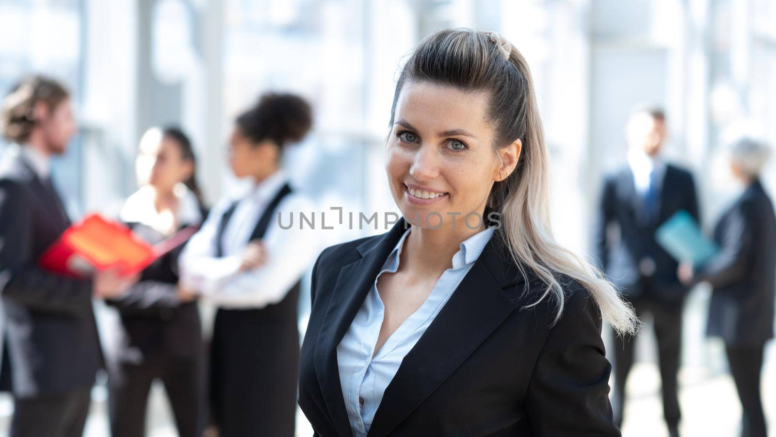 Beautiful young business woman in formal suit standing in front of colleagues in business building
