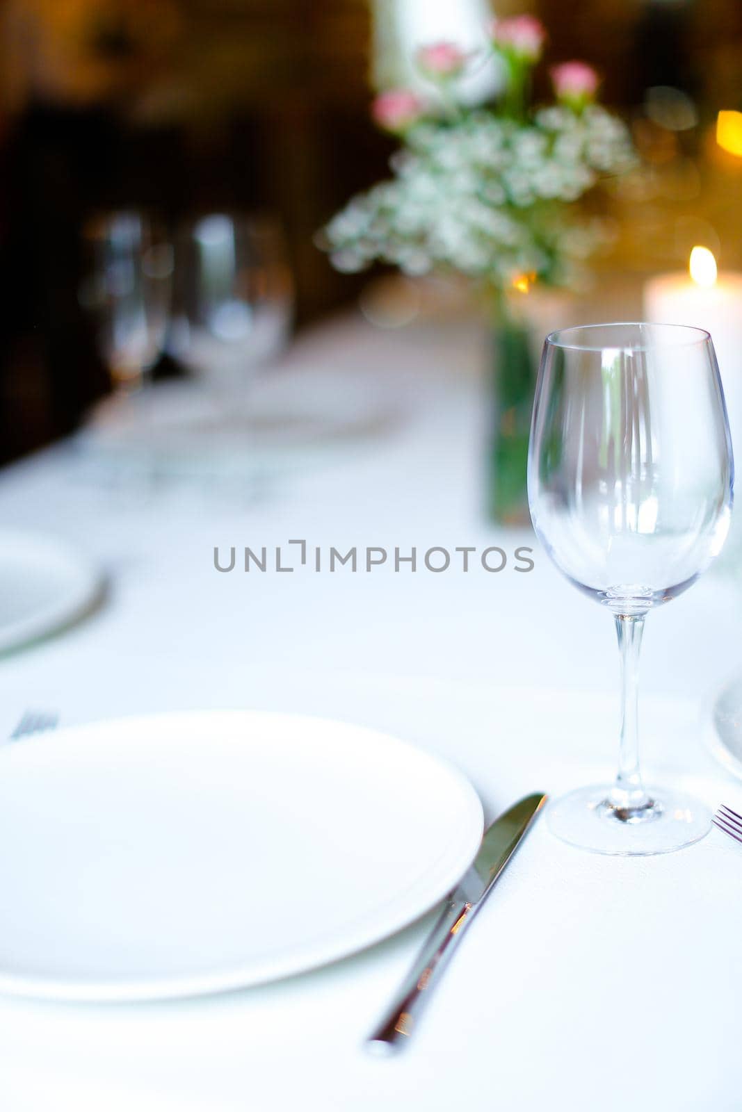 Bouquet of flowers, wineglass and candles on white table. oncept of romantic dinner and catering establishment.