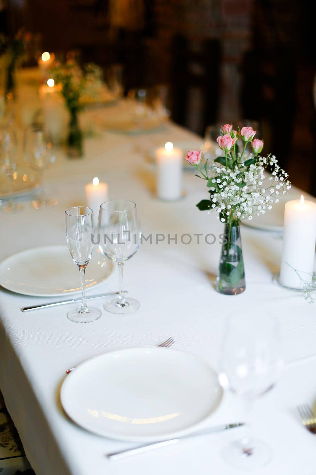 Bouguet of flowers, plates with forks and white candles on table. oncept of romantic dinner and catering establishment.