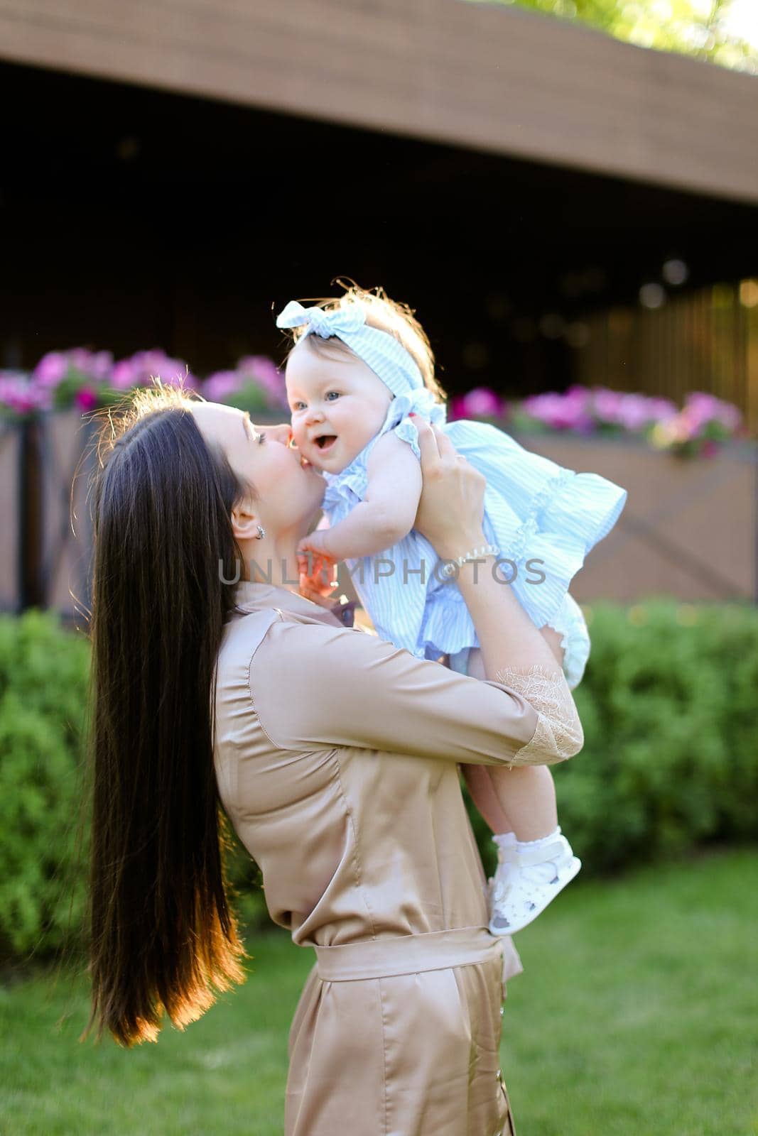 Young happy mother holding and kissing little daughter in grass background. Concept of motherhood and child.