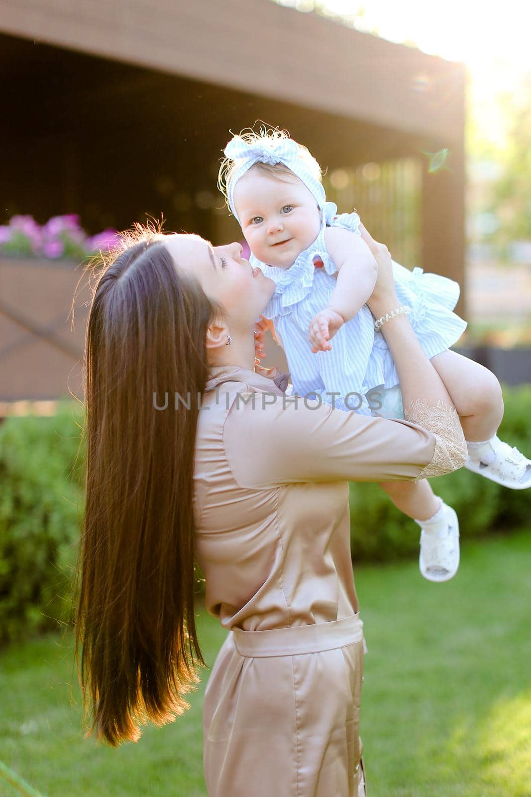 Young caucasian mother holding and kissing little daughter in grass background. Concept of motherhood and child.