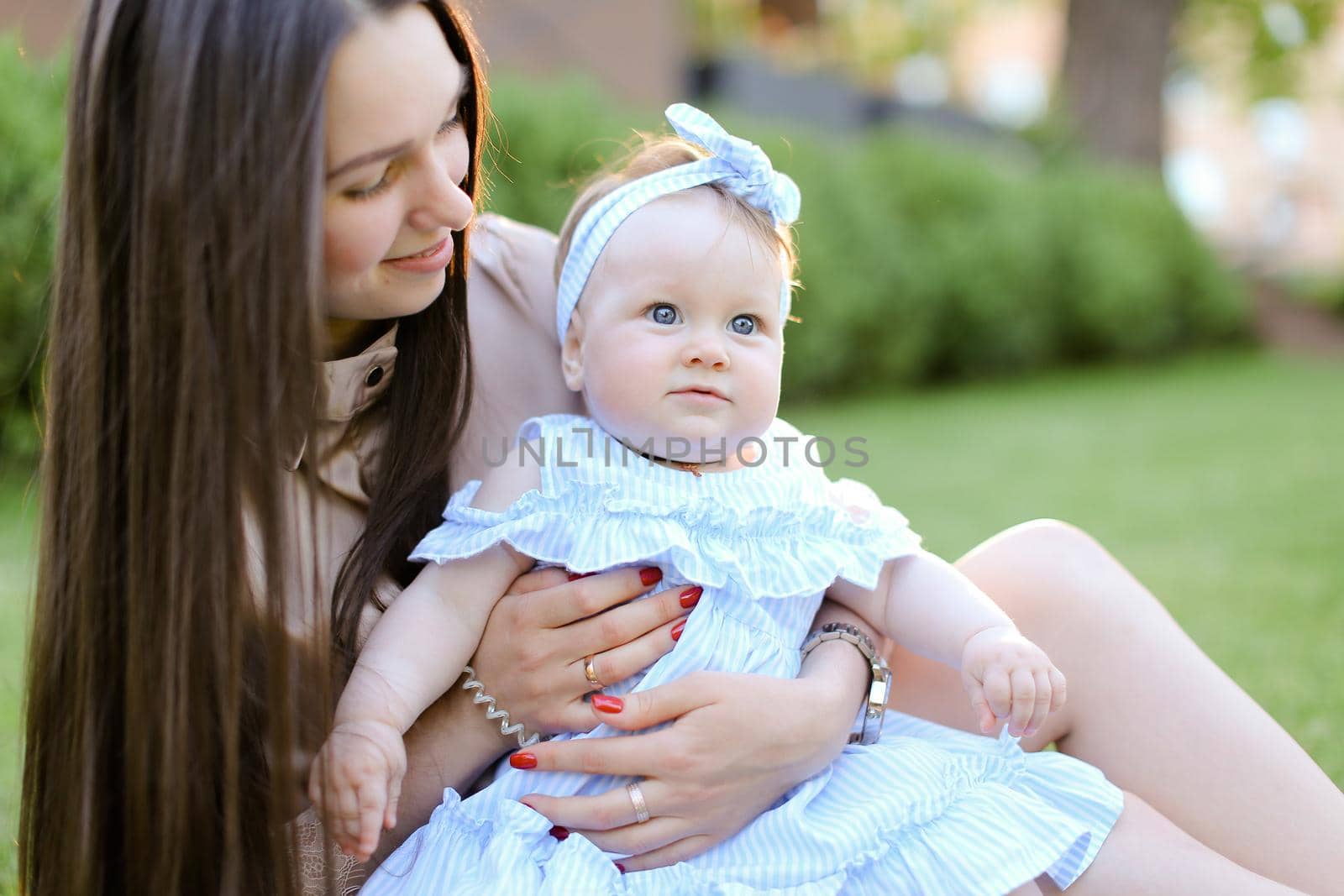 Young caucasian woman sitting on grass with little female baby. Concept of motherhood and children, resting on open air.