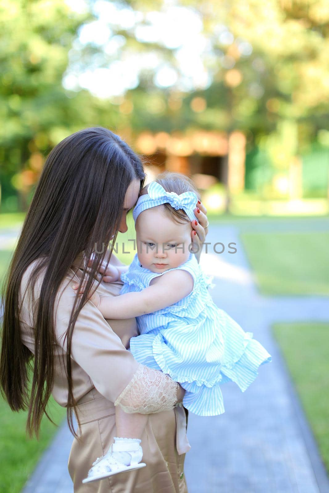 Young brunette mother holding little female child in garden. Concept of motherhood and resting on nature.