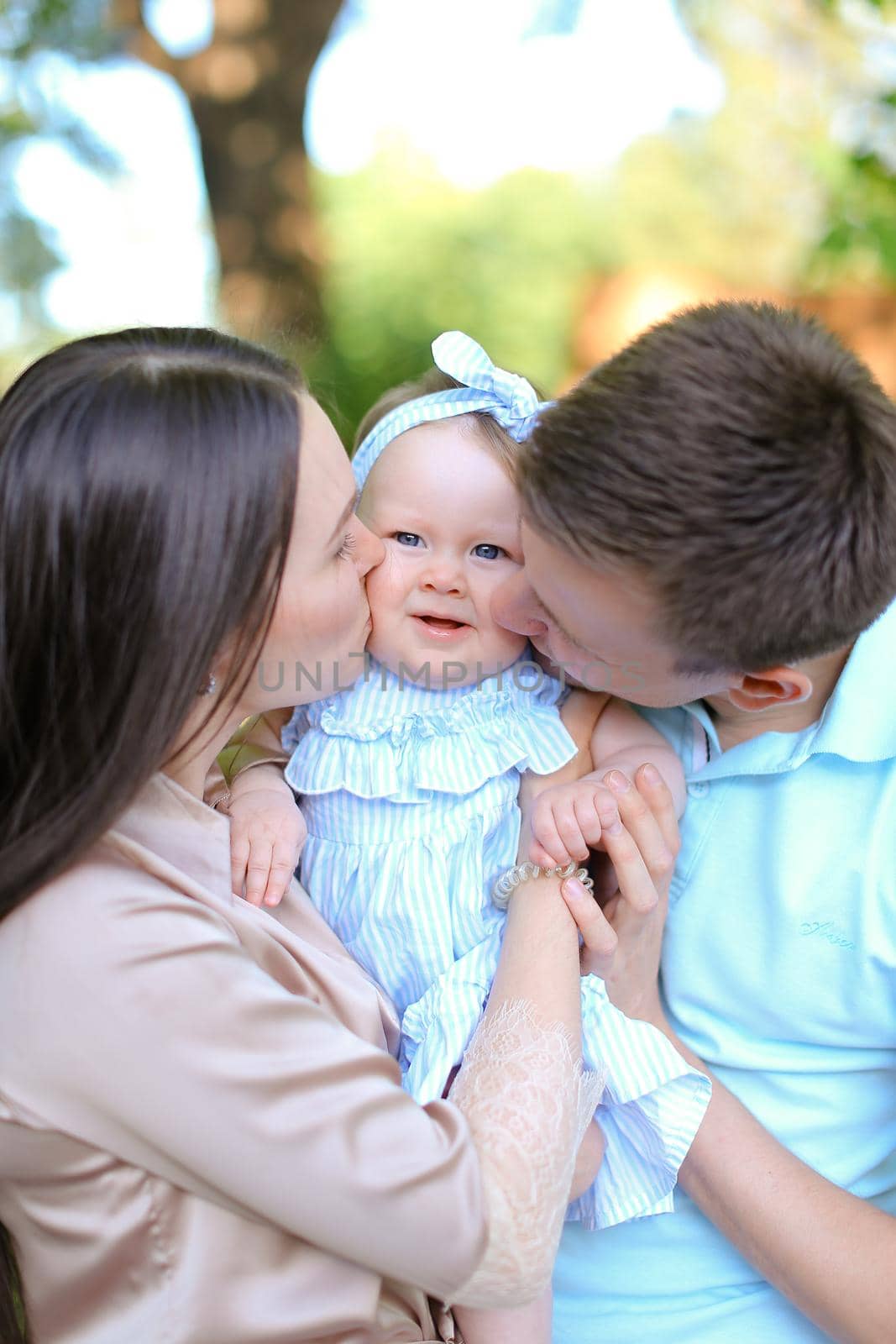 Young mother and father kissing little female baby. Concept of parenthood and child.