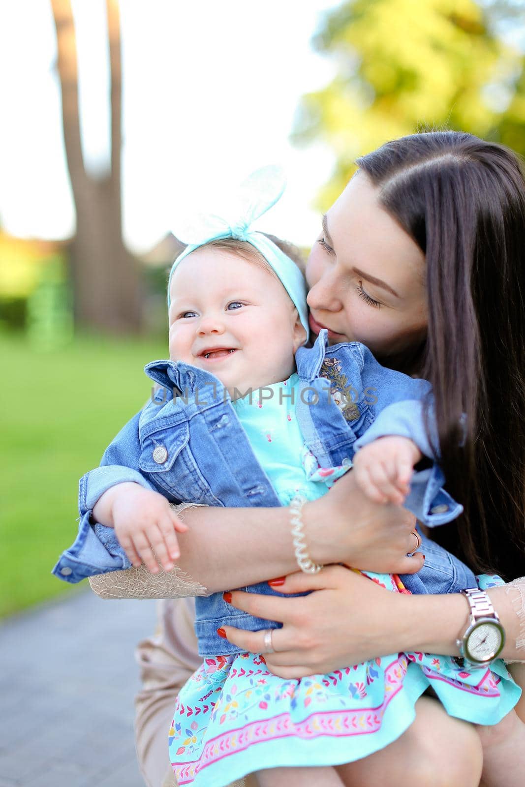 Young brunette woman holding little daughter wearing jeans jacket. Concept of motherhood and children.