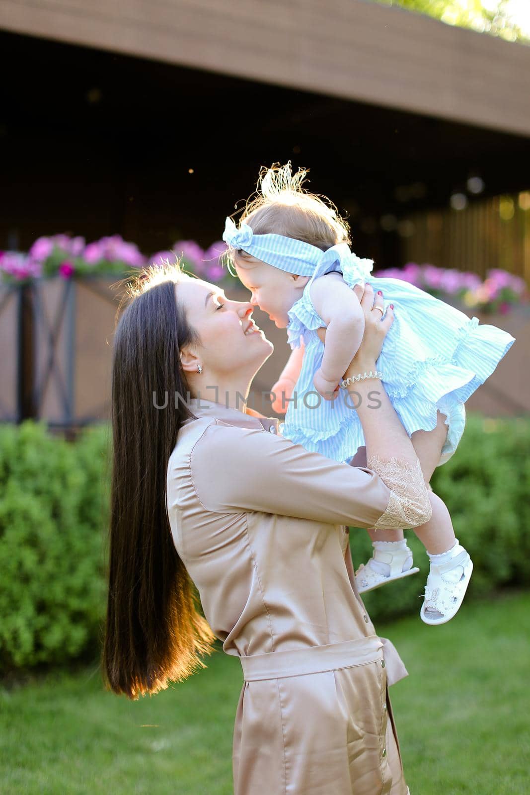 Young mother holding and kissing little daughter in grass background. Concept of motherhood and child.