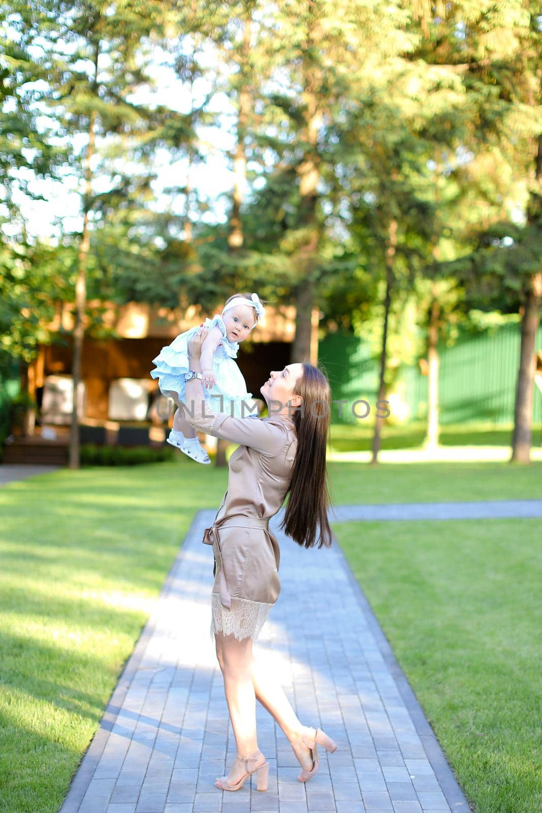 Young pretty mother wearing dress holding little baby in garden. Concept of motherhood and resting on open air in park.