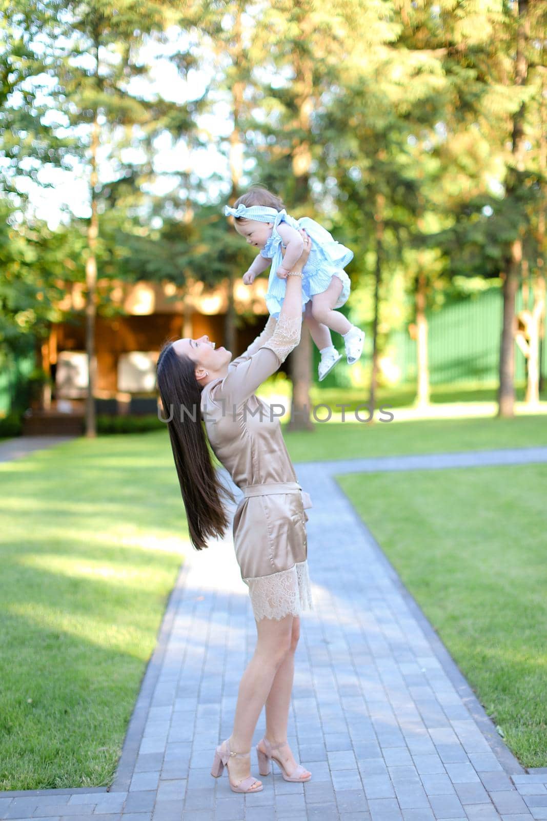 Young european woman wearing dress holding little baby in garden. by sisterspro