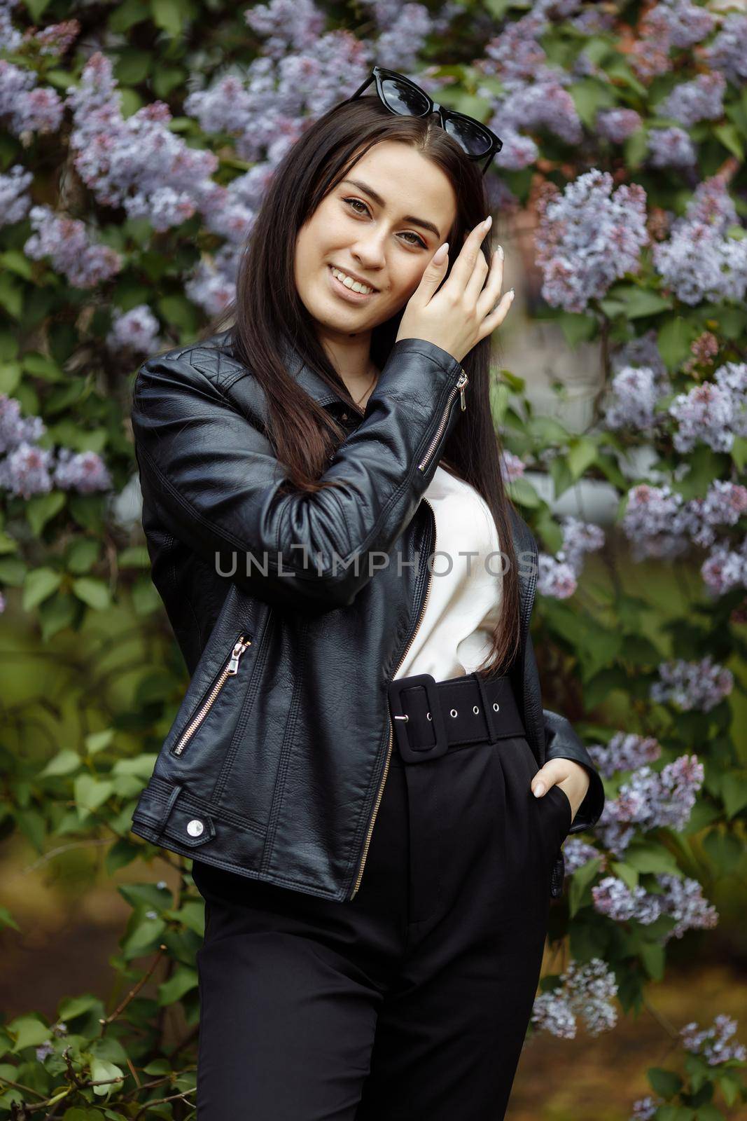 Laughing and smiling beautiful happy artistic young model girl with long hair in summer lilac garden with flowers posing for camera. Playing with hair concept.