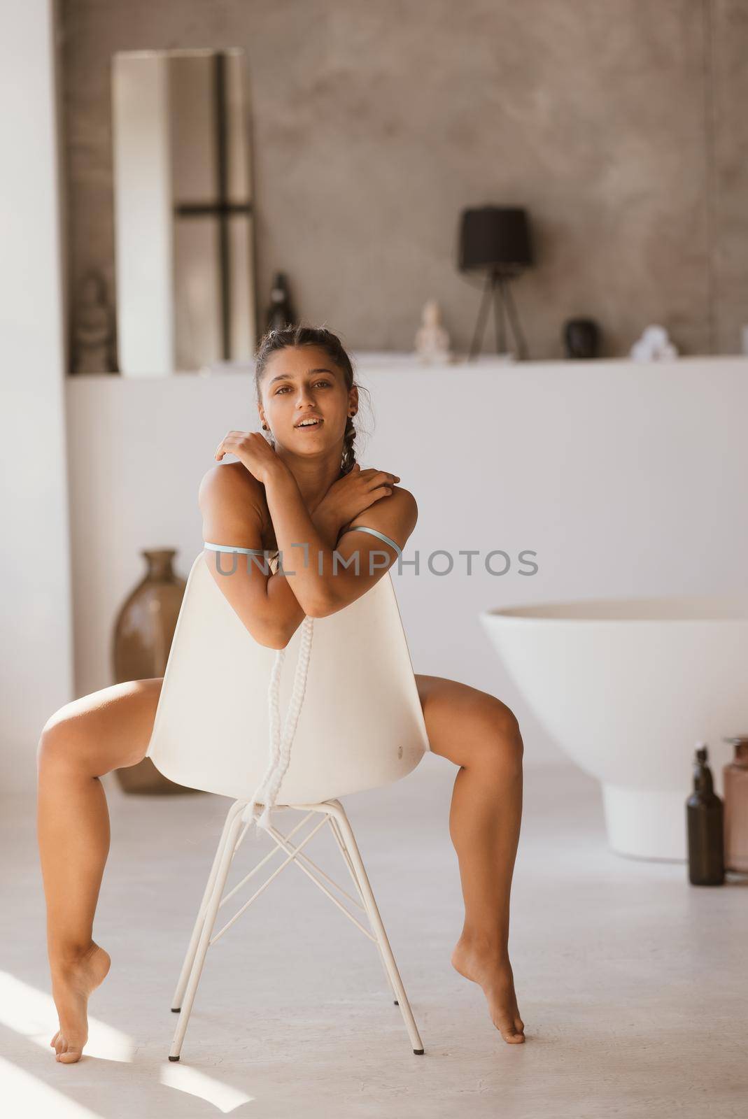 Girl in lingerie sits on a chair and looks at the camera. Poses at the camera.