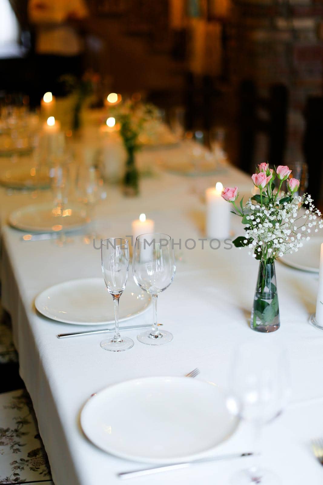 Bouguet of flowers, plates with forks and white candles on table. oncept of romantic dinner and catering establishment.