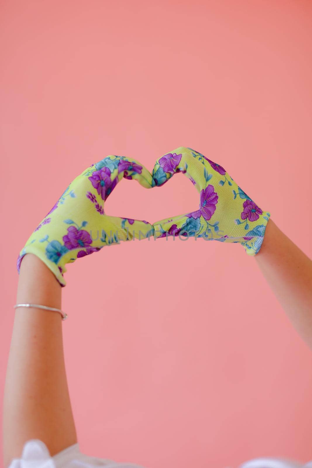 Closeup hands wearing gloves showing heart gesture by hands in pink monophonic background with copyspace. Concept of love and positive.