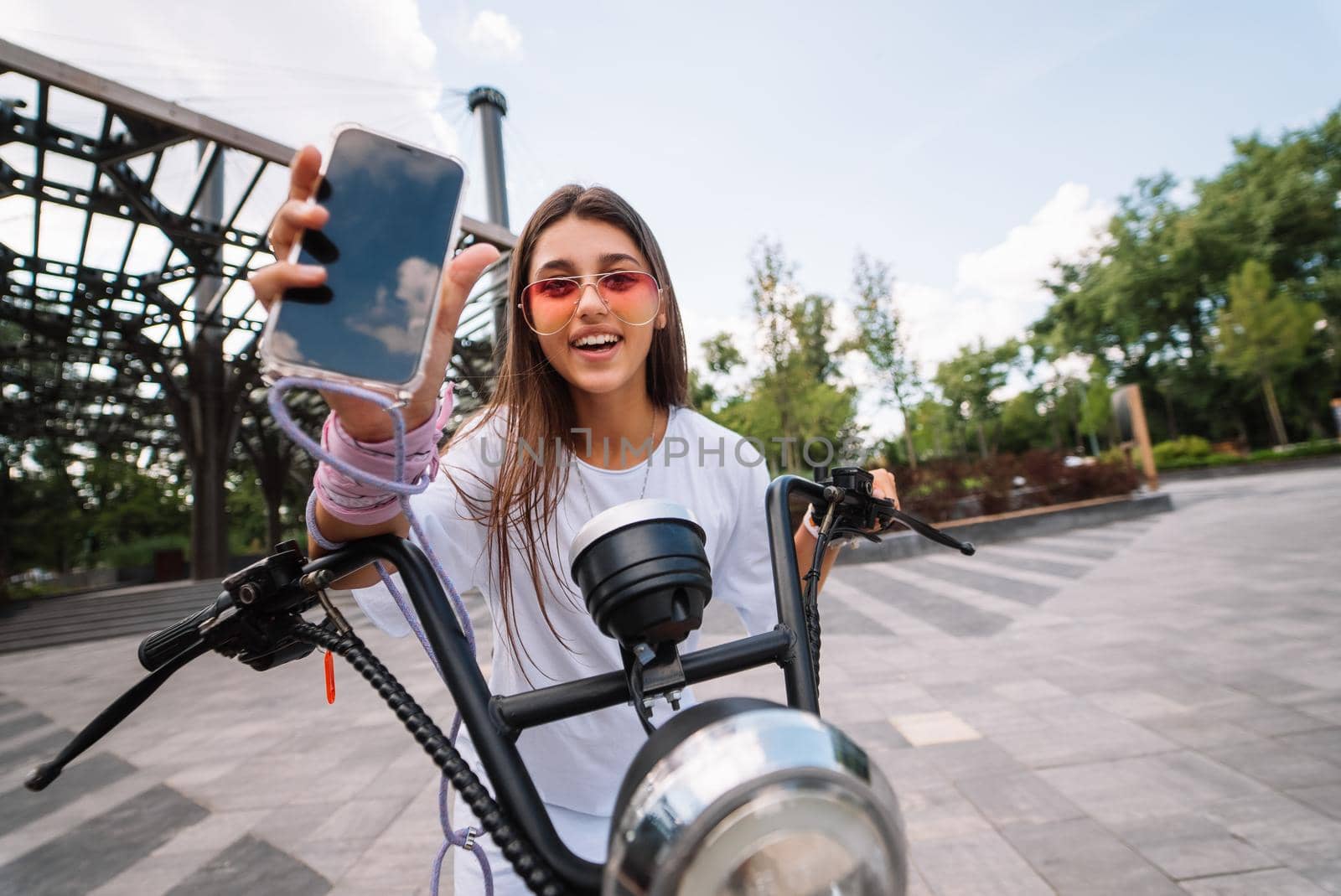 Girl sitting on a scooter and showing the phone to the camera, electric transport,