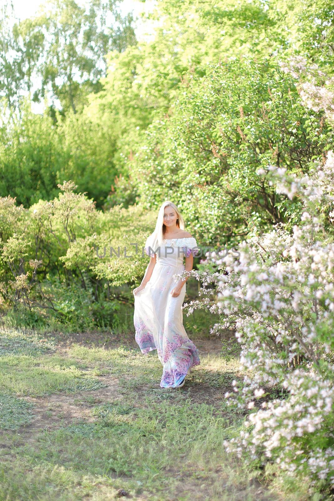 Young woman wearing white dress standing near white lilac flowers. by sisterspro