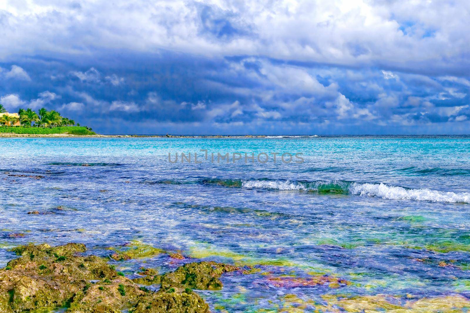 The view from the shore of a beautiful tropical sea with a beach. The warm waters of the ocean bathe colorful stones in the water. Vacation concept.