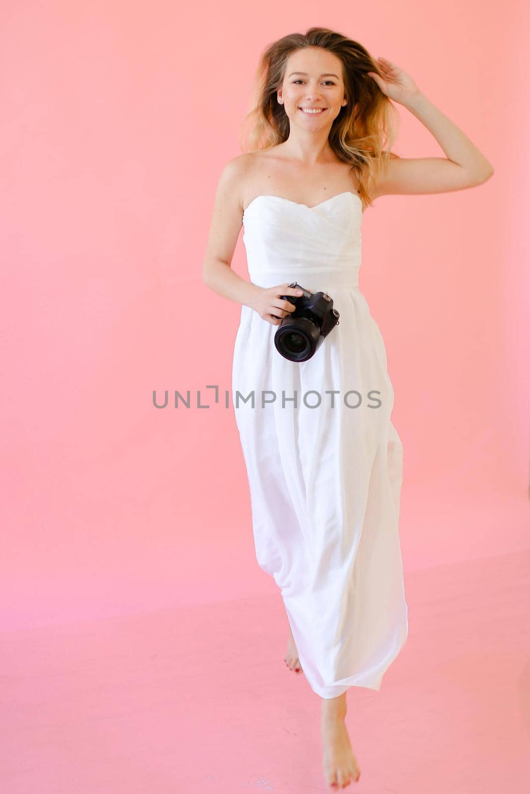 Young caucasian female photographer with camera in pink monophonic background. by sisterspro