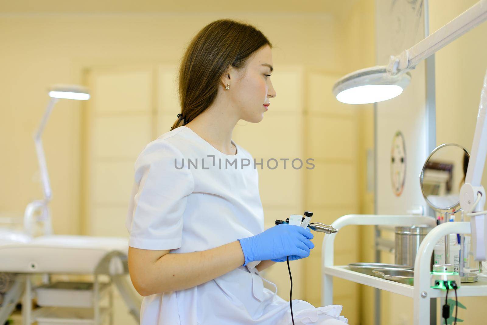 Young cosmetlogist standing with microblading device near mirror at beauty salon. by sisterspro