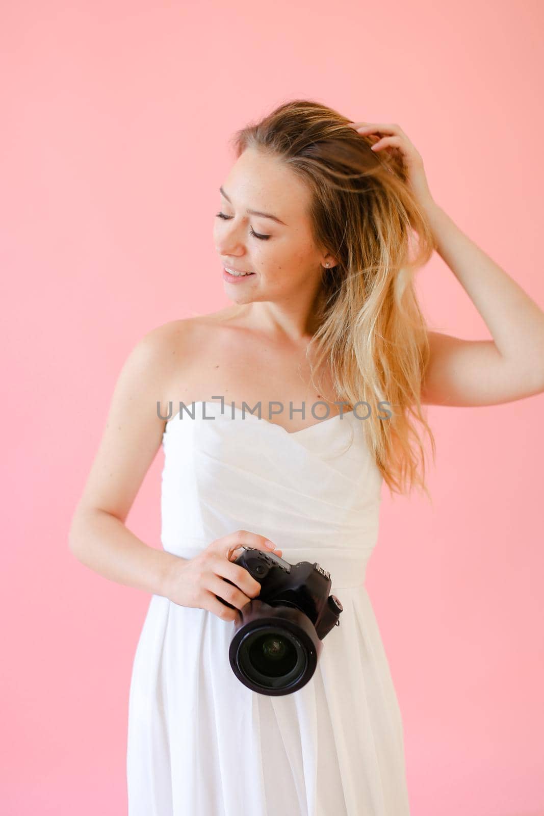 Young nice female photographer with camera in pink monophonic background. Concept of modern profession and photo session.