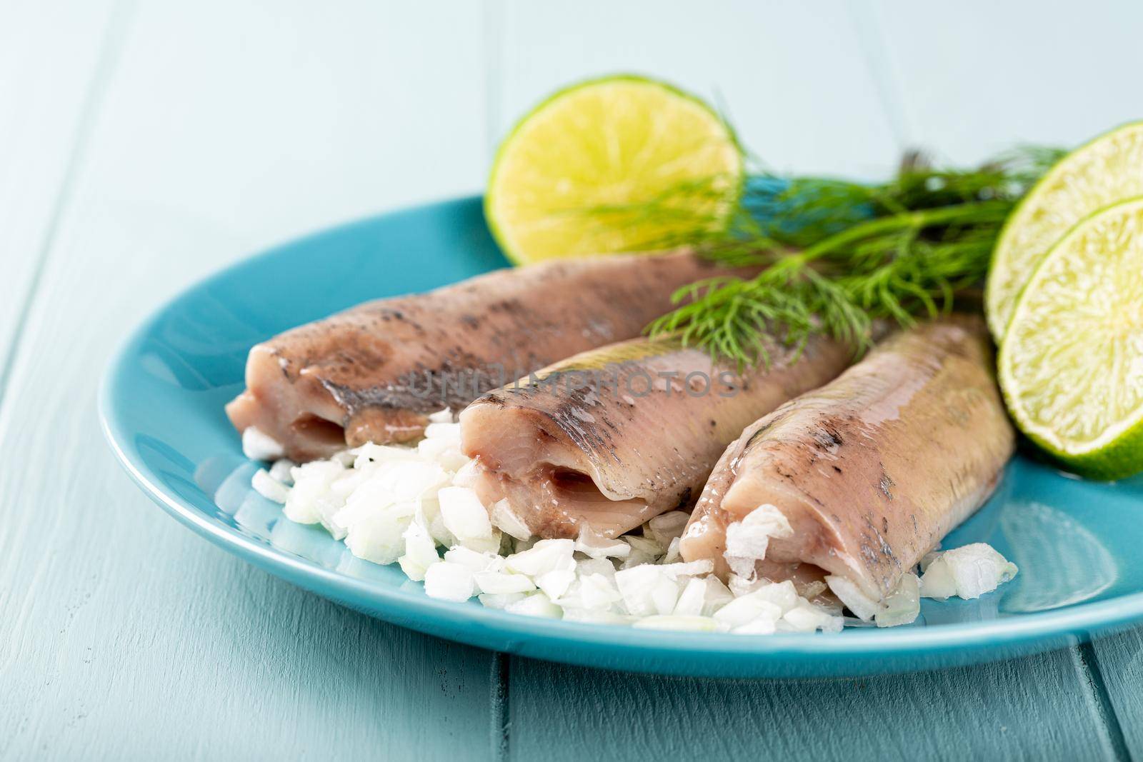 Traditional dutch food freshly salted herring fish with onion called hollandse nieuwe on turquoise plate and wooden background. European food concept with copy space.