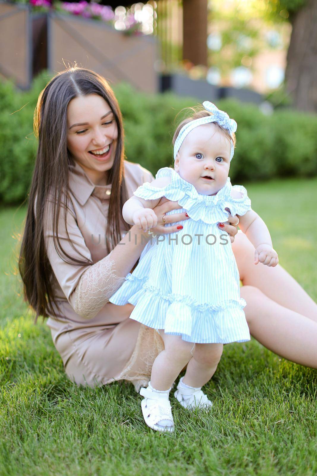 Young smiling woman sitting on grass with little female baby. Concept of motherhood and children, resting on open air.