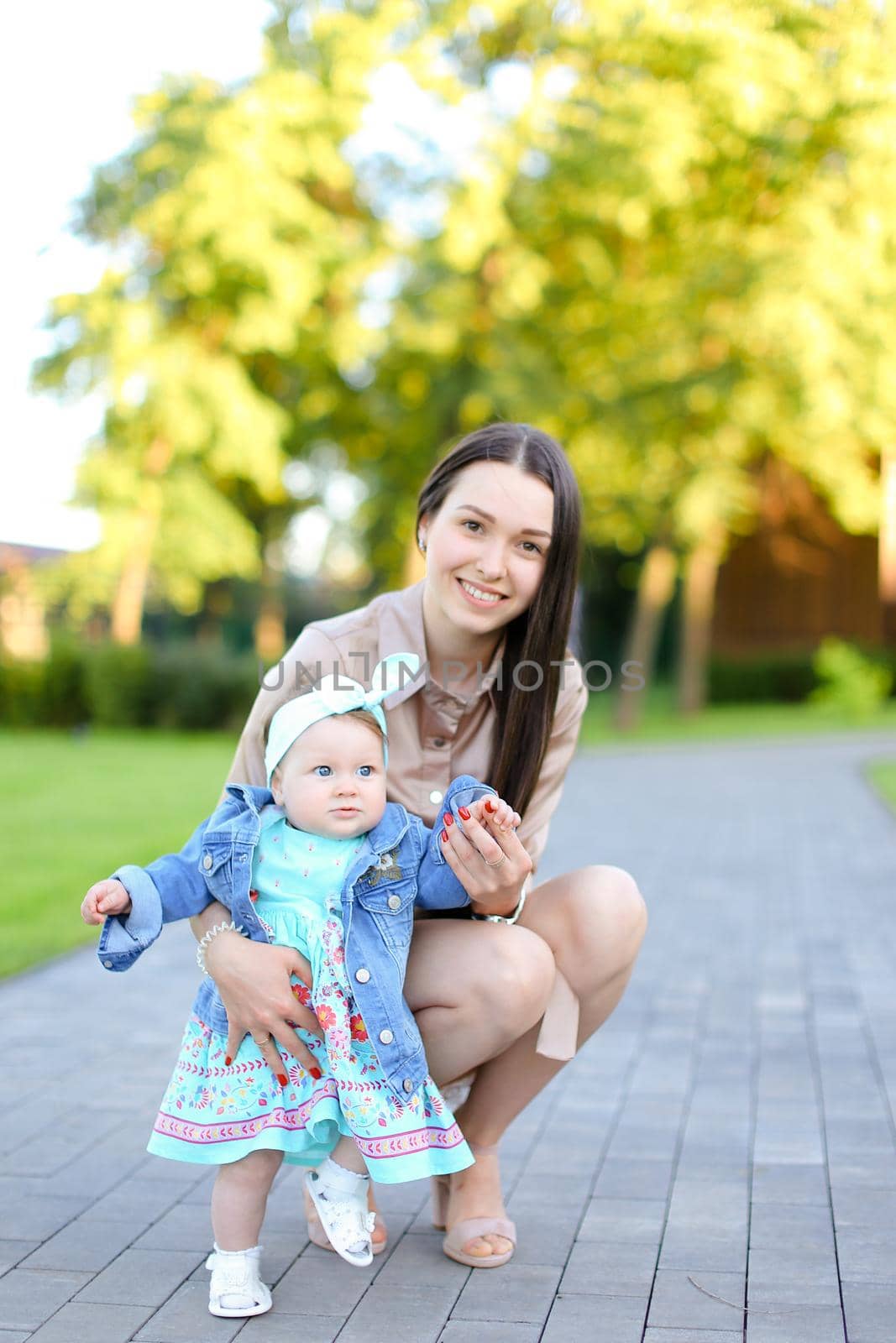 Young smiling mother walking with little daughter in park. Concept of female child and motherhood.