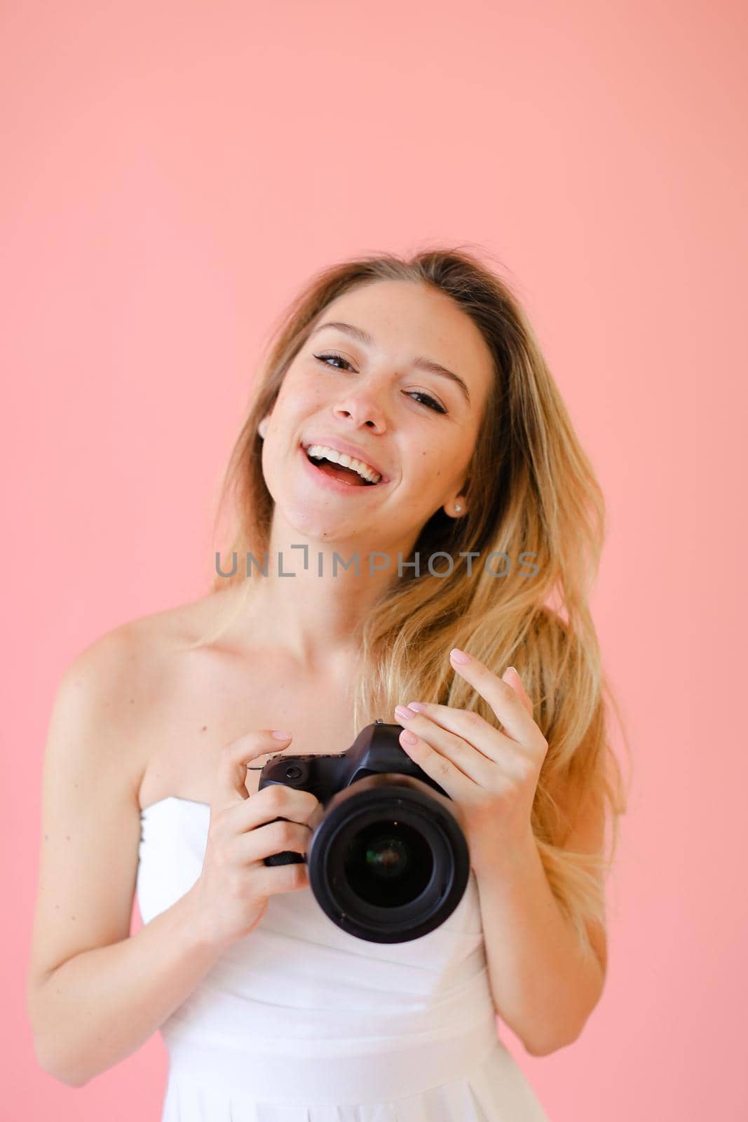 Closeup young jocund female photographer with camera in pink monophonic background. by sisterspro