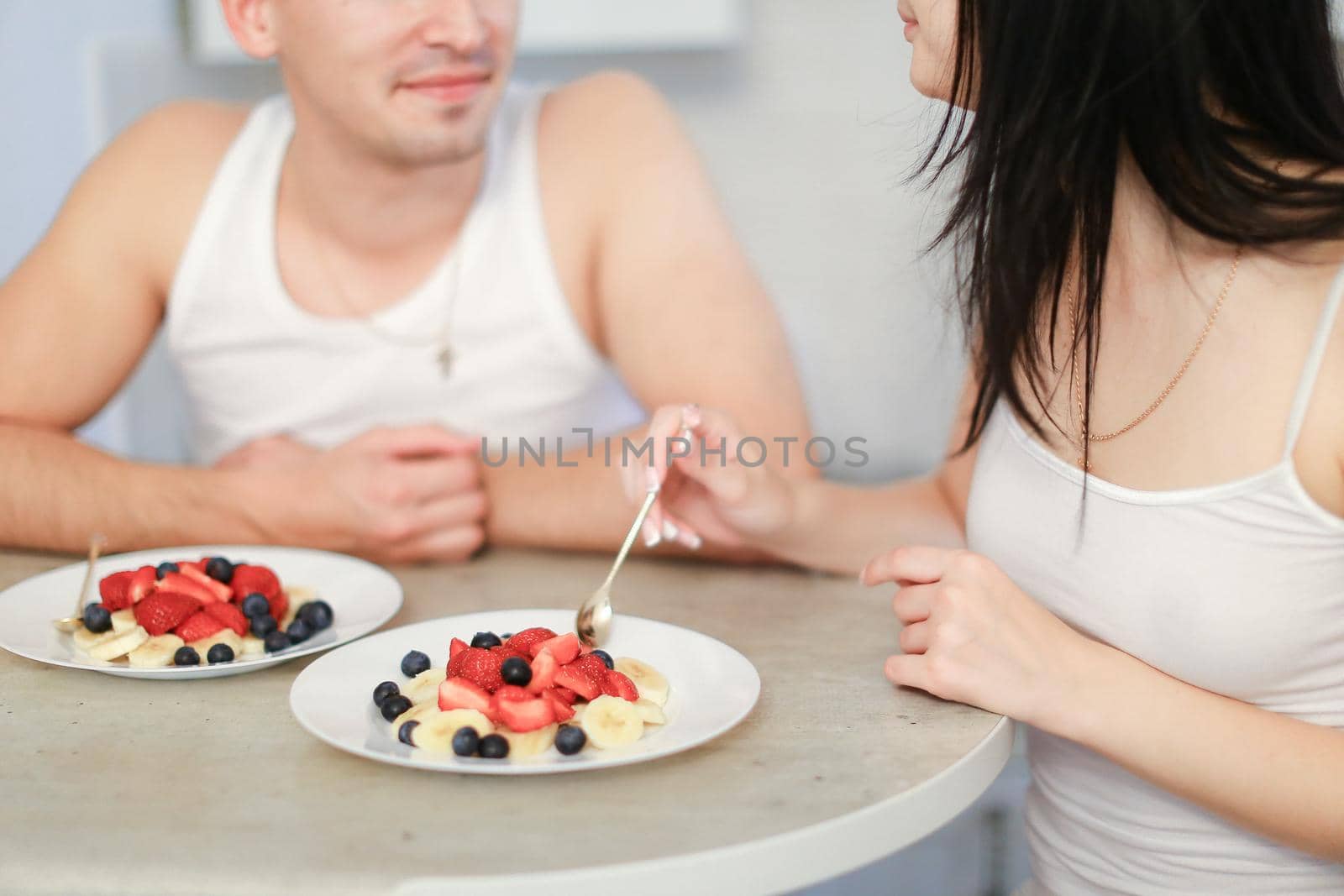 Husband and wife having breakfast in kitchen, two plates with porridge and berries. by sisterspro