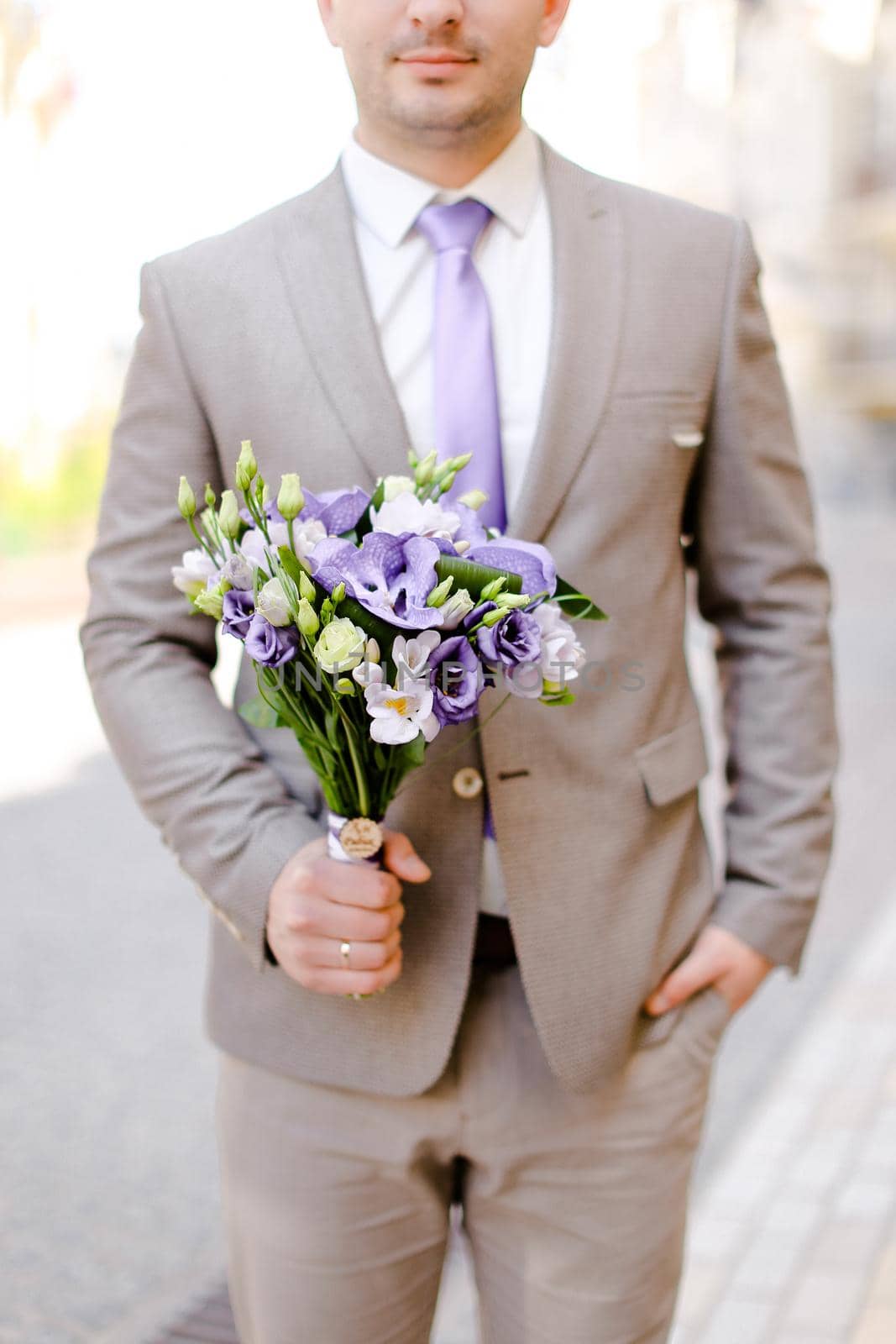 Young caucasian groom keeping bouquet of flowers and wearing grey suit. by sisterspro