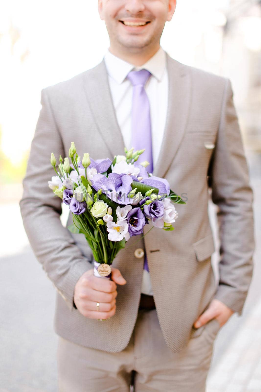 Young caucasian groom keeping bouquet of flowers and wearing grey suit. Concept of wedding photo session and waiting for bride.