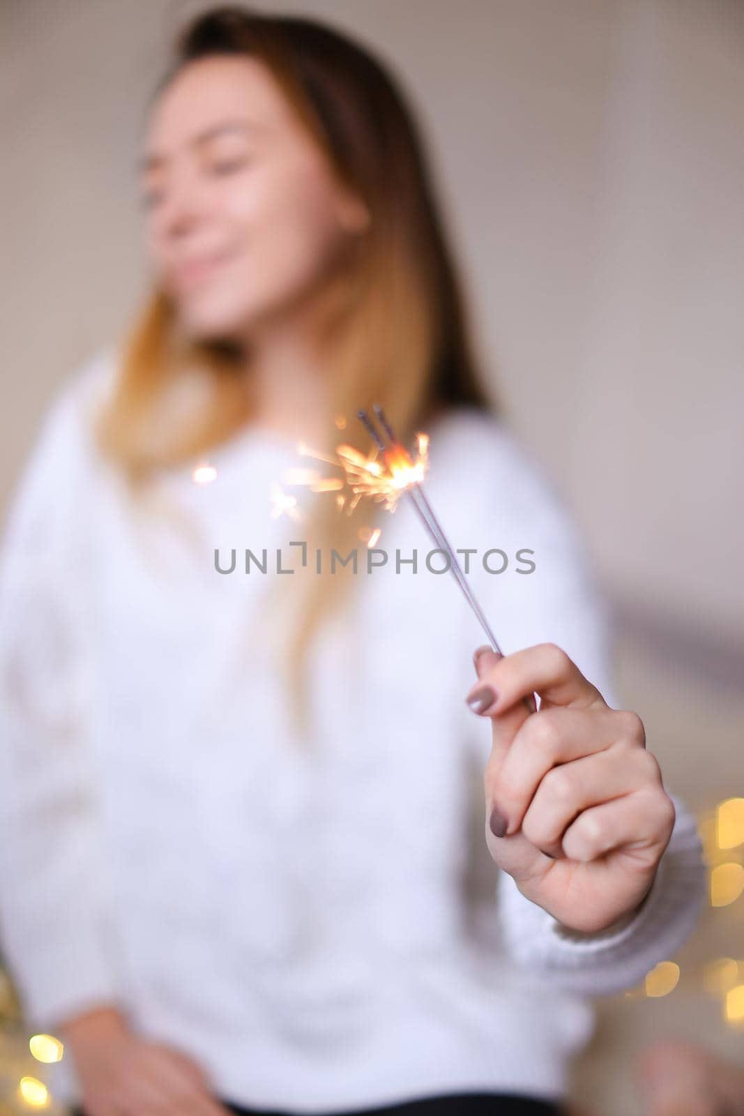 Blurred photo of young happy woman sitting with closeup bengal light near twinkling yellow garlands. by sisterspro