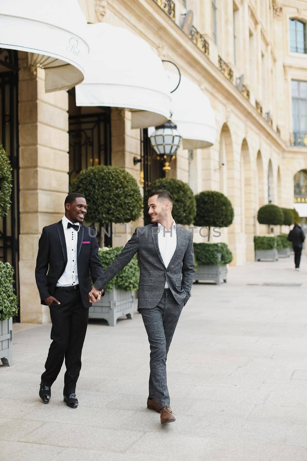 Afro american and caucasian happy handsome gays walking outside and holding hands in city. Concept of same sex male couple.