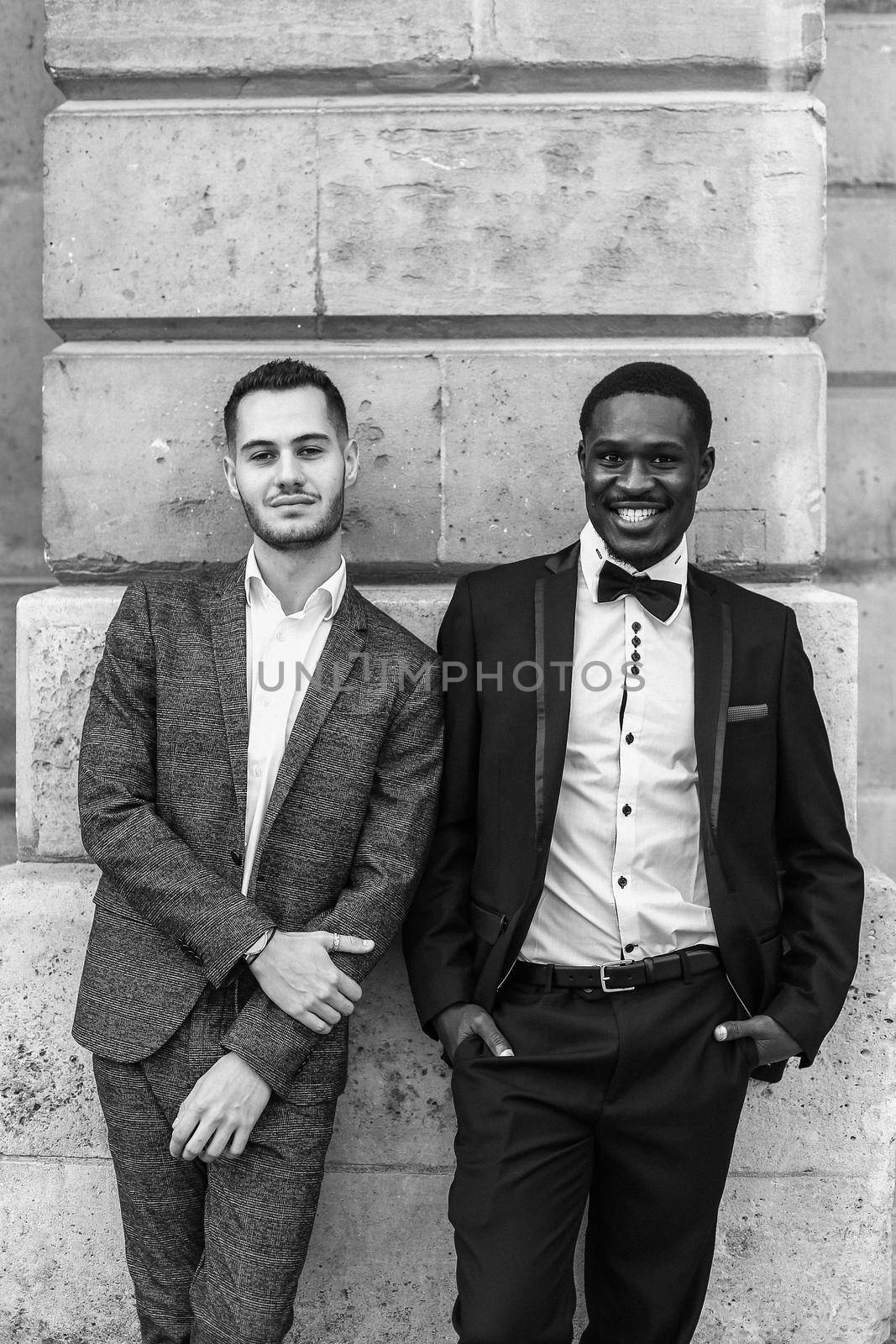 Black and white bw portrait in Paris Afro american and caucasian happy gays in suits standing near building. by sisterspro