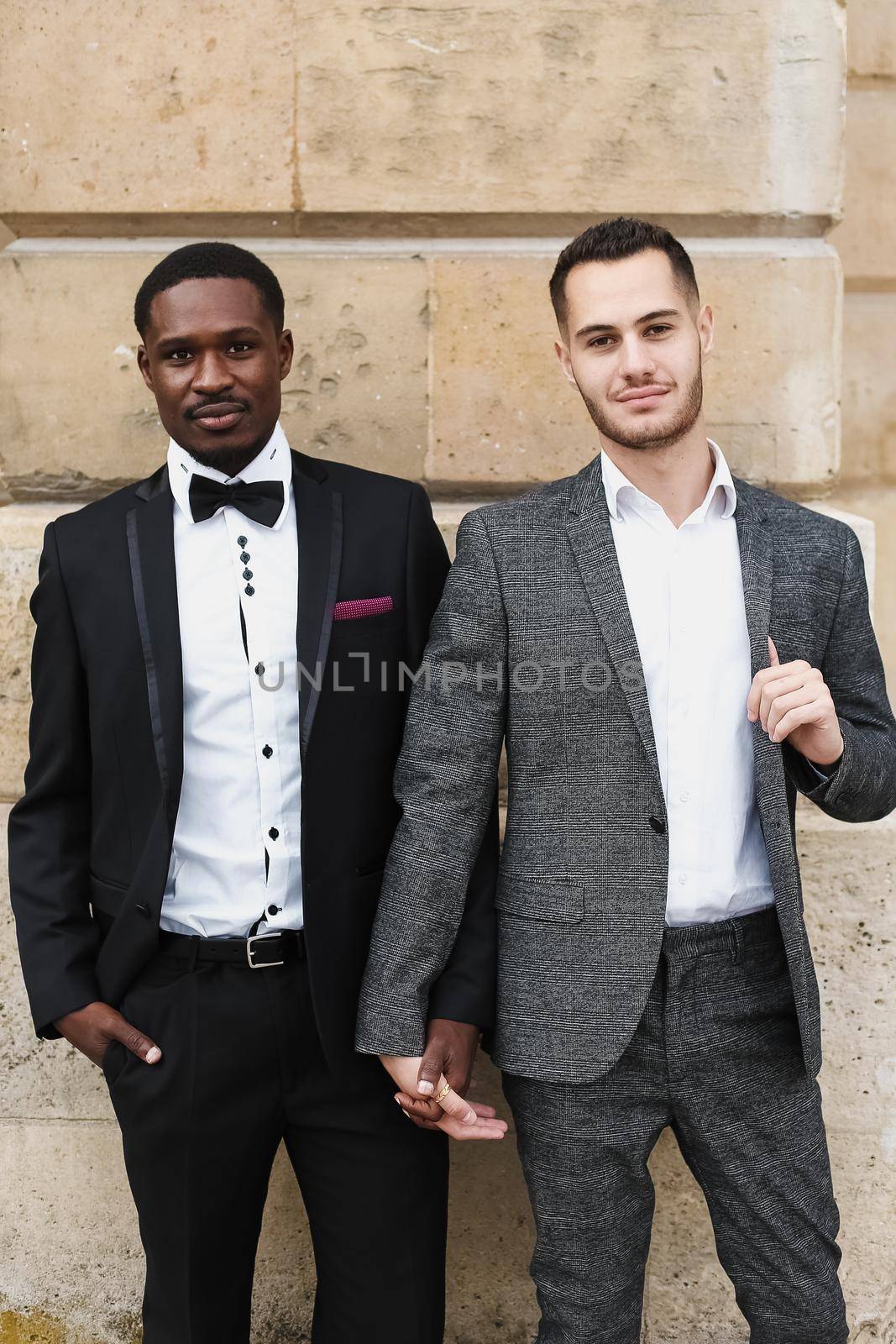 Afro american and caucasian happy lgbt gays in suits standing near building. by sisterspro