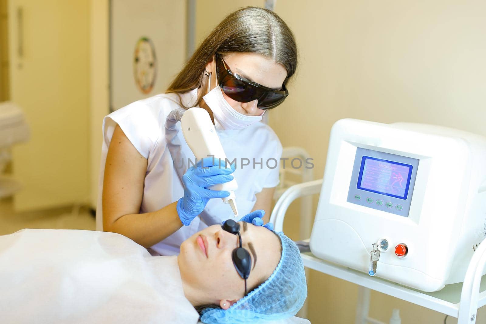 Young cosmetologist removing permanent makeup with laser for young girl at beauty salon. Concept of cosmetology equipment, special procedure before microblading.