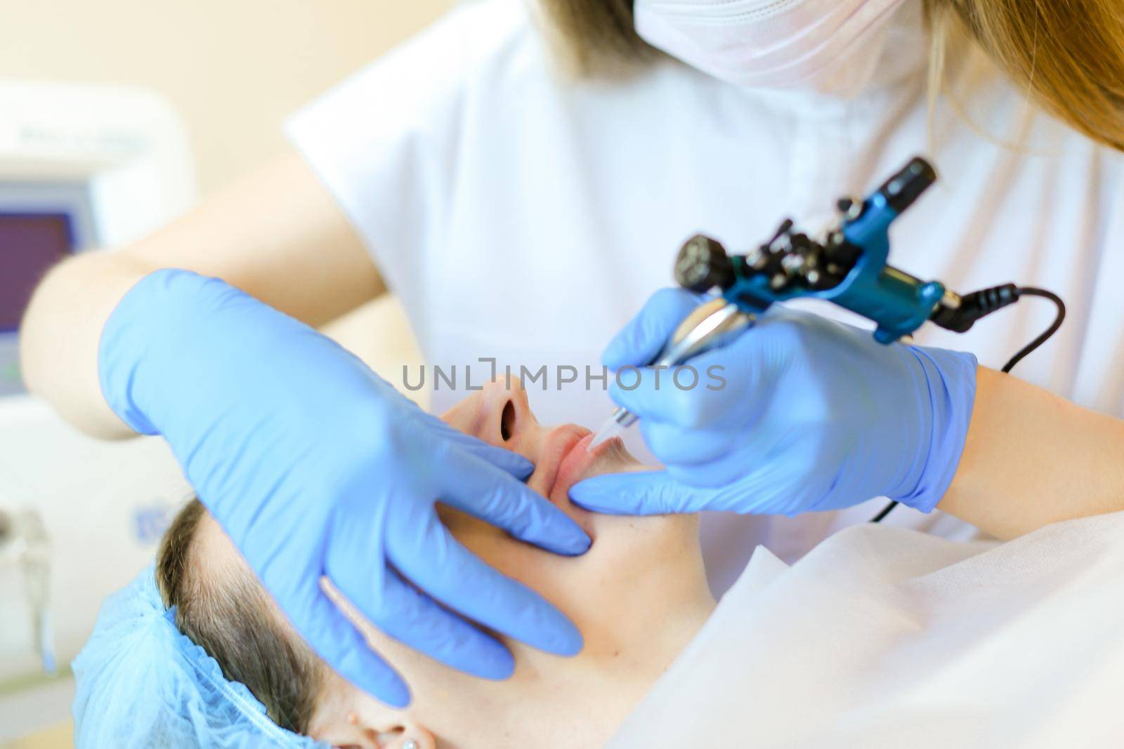 Close up hands in blue latex gloves making lip tattoo with microblading device. Concept of beauty salon, permanent makeup and cosmetology equipment.