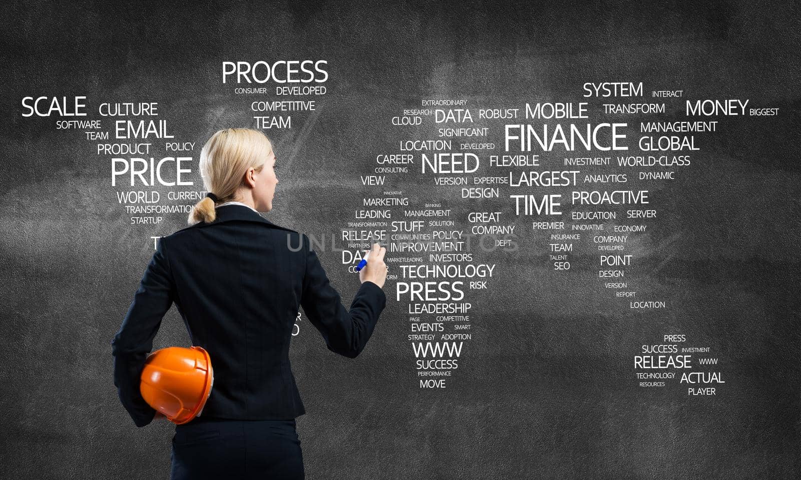 Businesswoman standing near world map consists of business terms on concrete wall. International company business presentation. Back view woman speaker with safety helmet and marker pen in hands.