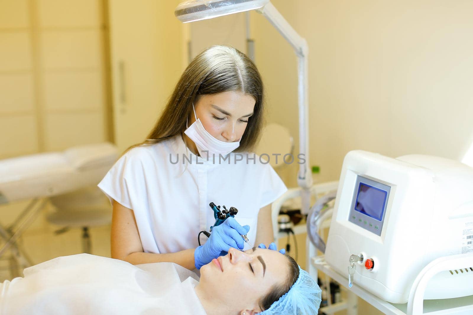 Caucasian cosmetologist making permanent makeup for girl at beauty salon. Concept of cosmetology equipment and microblading.