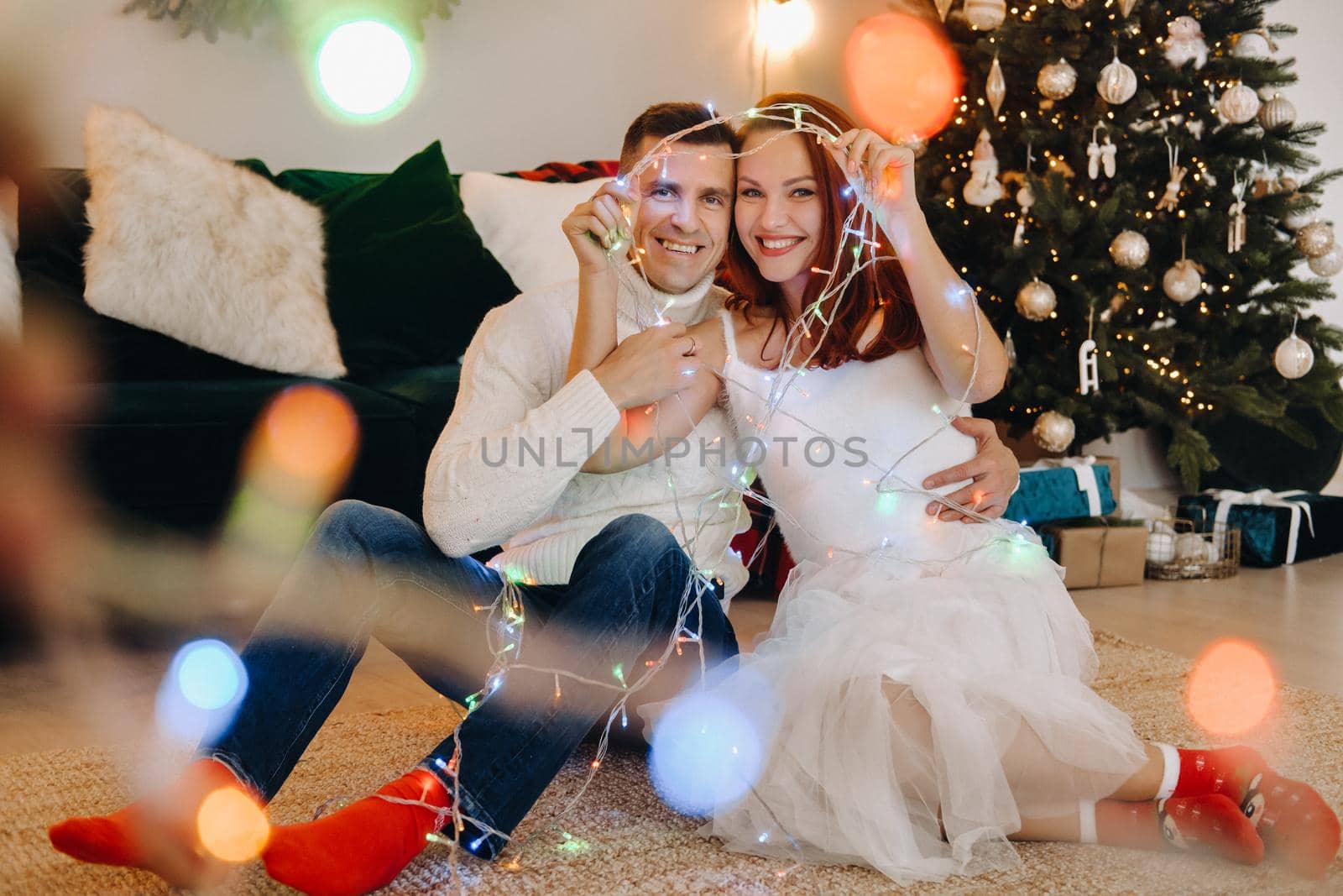 a happy married couple is sitting at home on the floor near the Christmas tree.