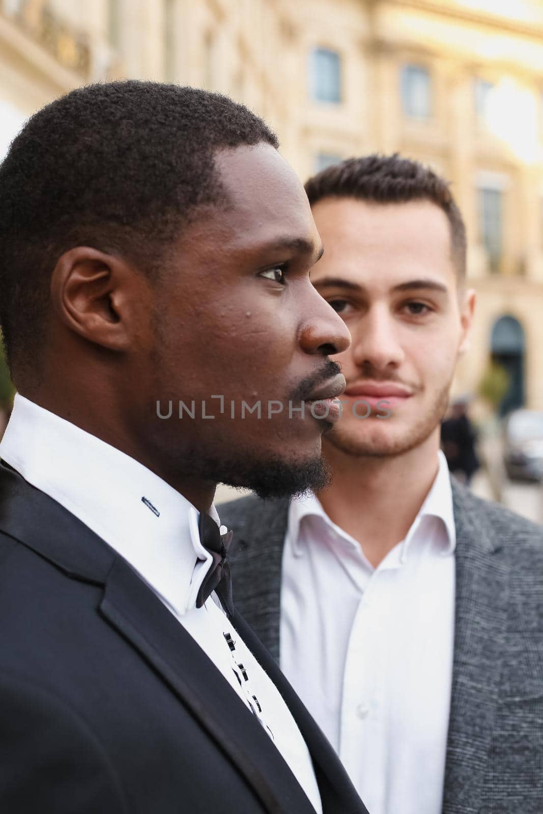 close up portrait of same sex couple. caucasian man wearing suit standing near afro american boy. Concept of business and male fashion.